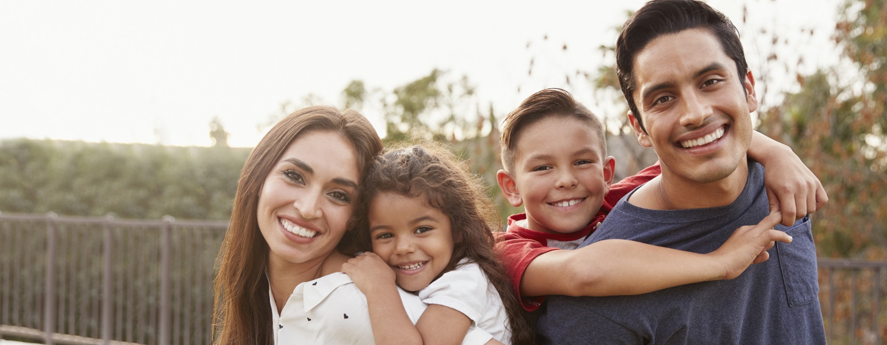 Young Hispanic parents piggyback their children in the park, smiling 