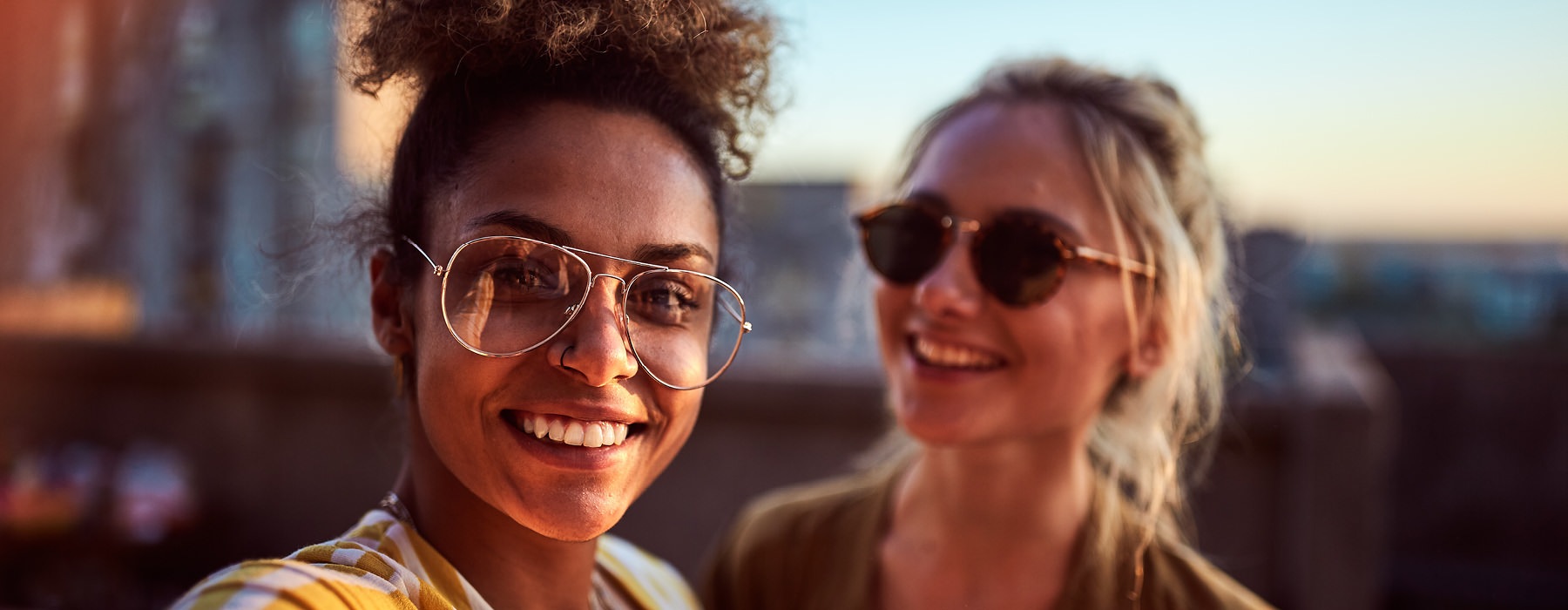 two women with sunglasses smile on building's rooftop